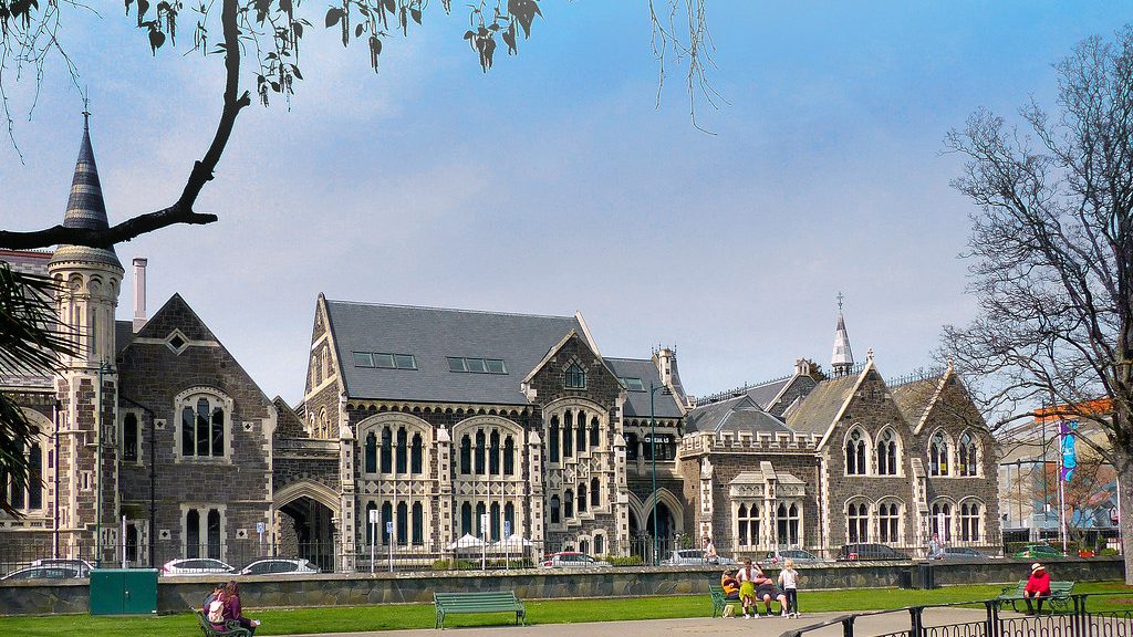 Stone university buildings with gabled roofs behind a lawn and walkway