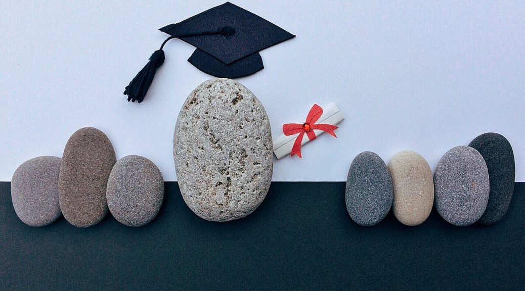 Stones arranged with a graduation cap and a diploma tied with a red ribbon.