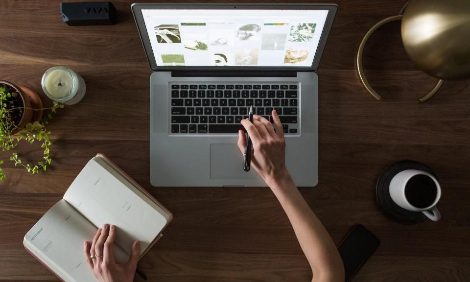 Overhead view of hands on a laptop and an open notebook on a wooden desk