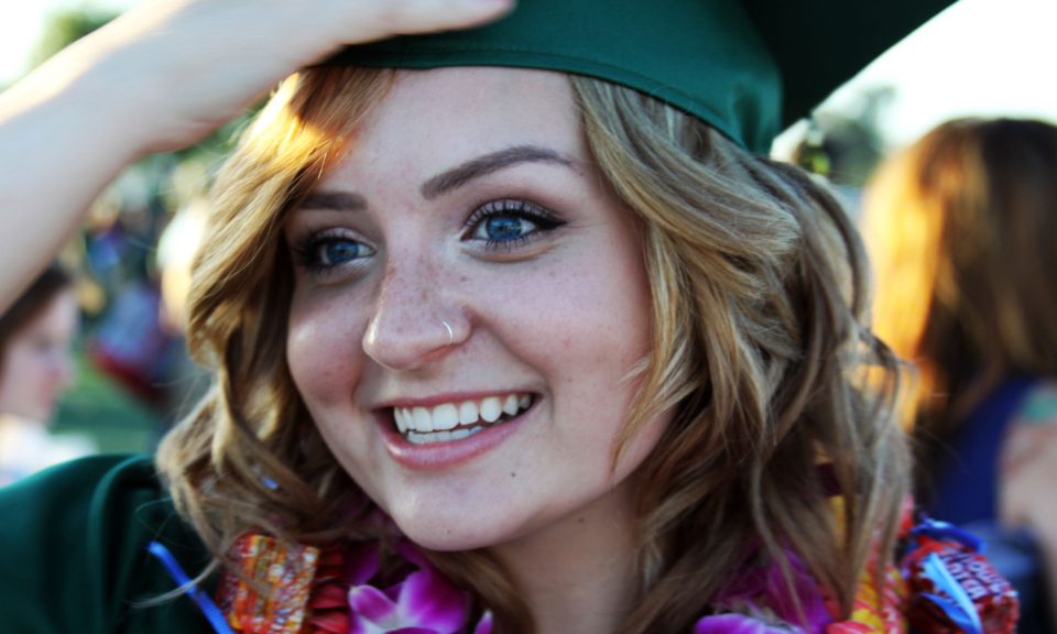 A smiling graduate in a green cap and flower lei at a ceremony