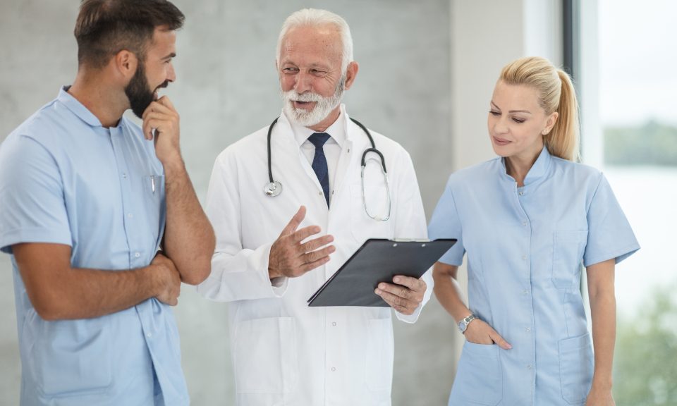 A doctor and two nurses in scrubs discussing notes on a clipboard